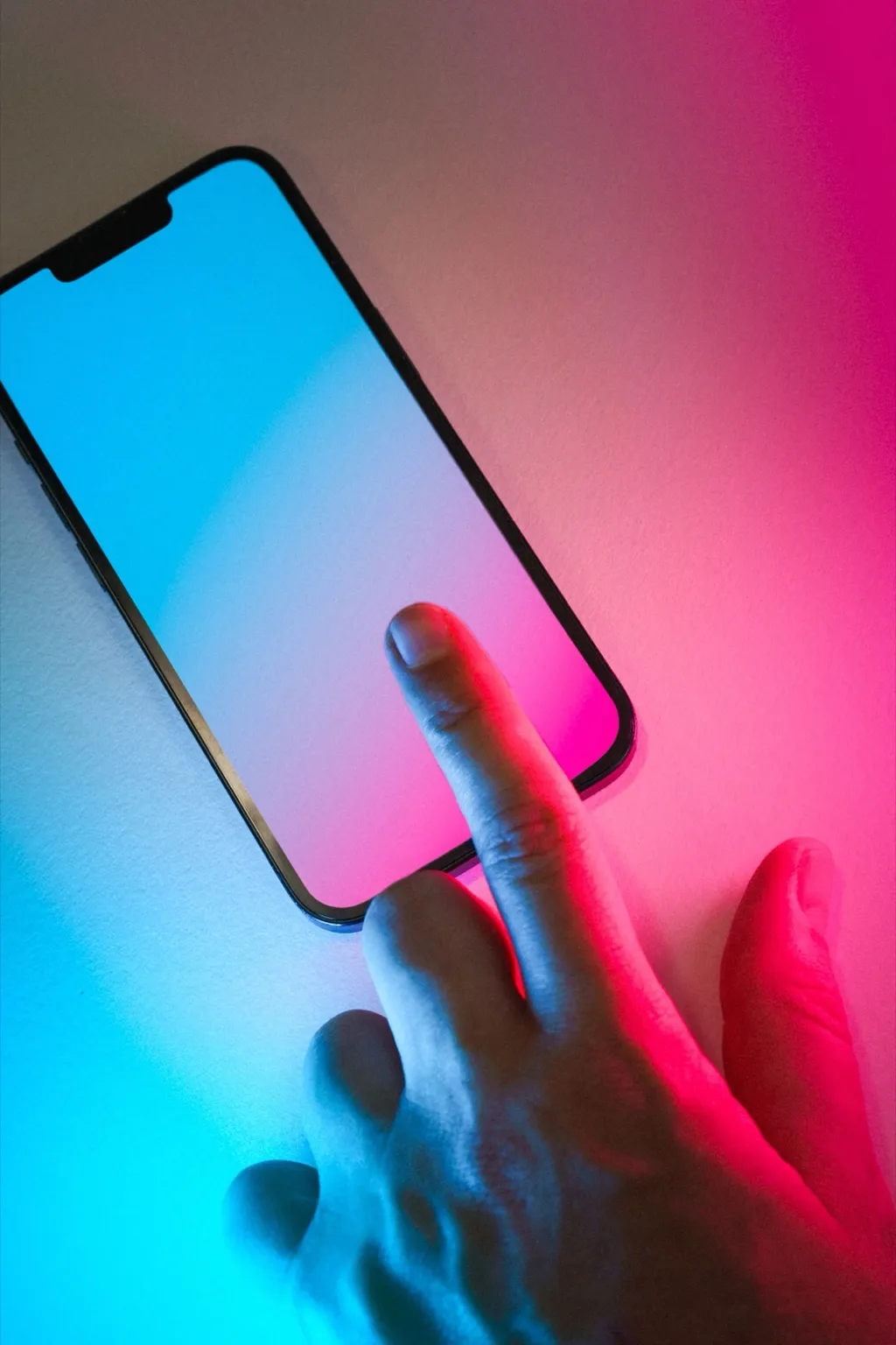 Finger touching a smartphone screen lit in blue and pink neon